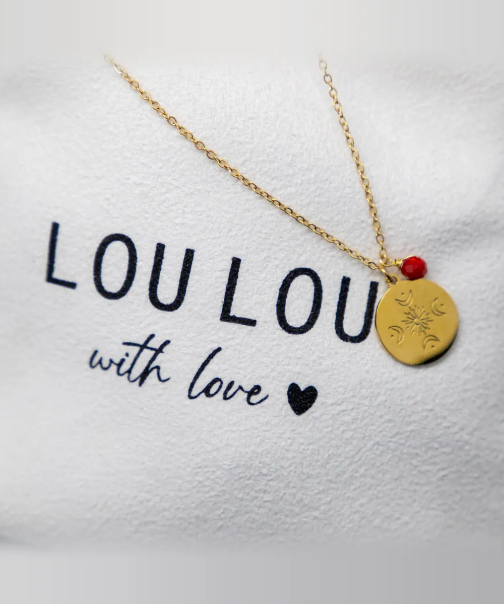 Collar con medalla de sol y lunas y cuenta roja sobre la bolsita LouLou with love